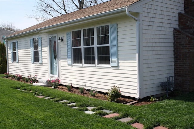 exterior space with roof with shingles and a yard