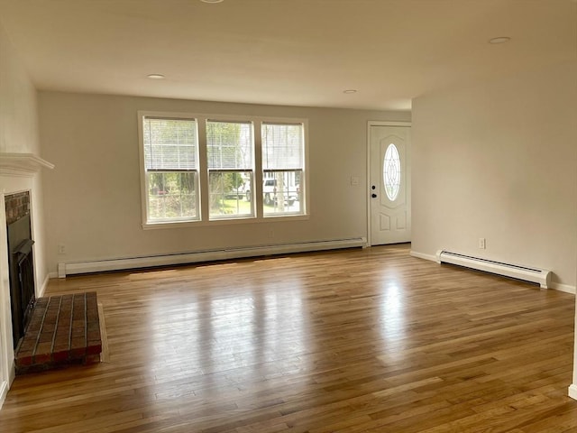 unfurnished living room featuring baseboards, a fireplace, a baseboard heating unit, and wood finished floors