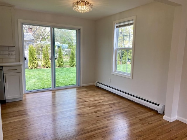 unfurnished dining area with light wood-style floors, baseboards, a baseboard radiator, and a wealth of natural light