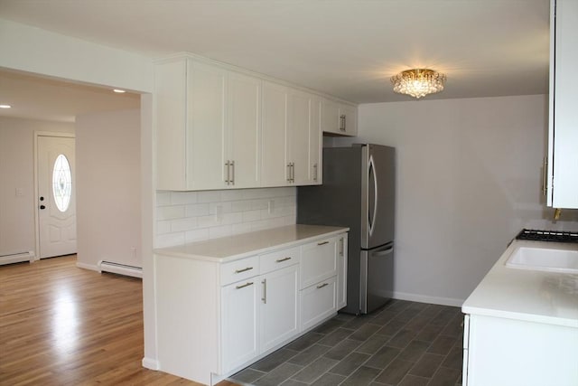 kitchen featuring freestanding refrigerator, baseboard heating, light countertops, tasteful backsplash, and a sink