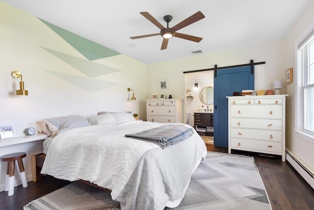 bedroom with visible vents, dark wood finished floors, a barn door, a baseboard radiator, and ensuite bath