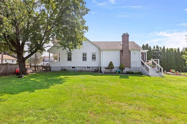 rear view of house featuring fence, a chimney, and a lawn