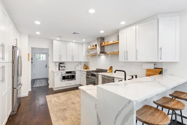 kitchen featuring visible vents, light stone countertops, a peninsula, stainless steel appliances, and wall chimney exhaust hood