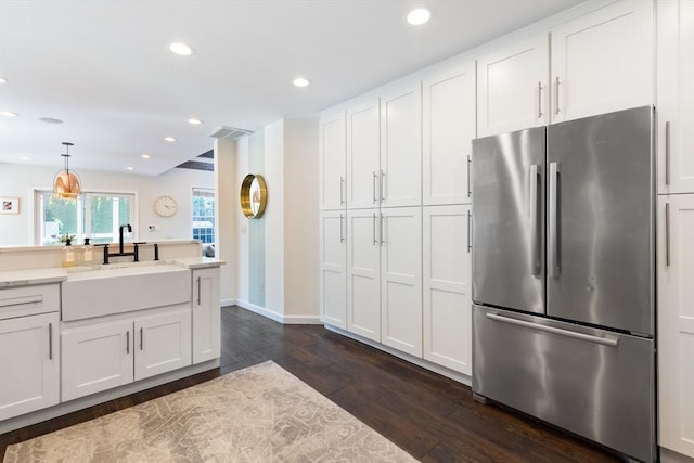 kitchen with a sink, freestanding refrigerator, white cabinetry, baseboards, and dark wood-style floors