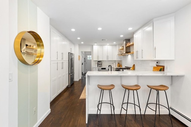 kitchen featuring wall chimney range hood, baseboard heating, freestanding refrigerator, a peninsula, and recessed lighting