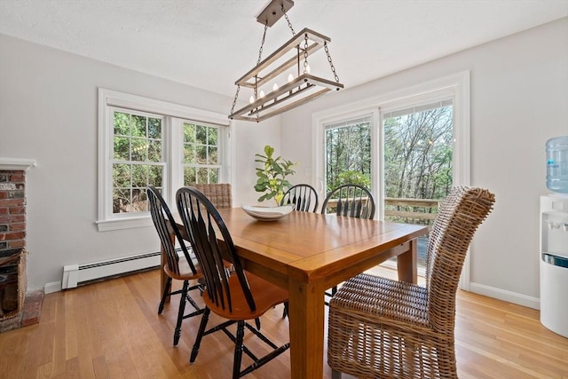 dining area with a baseboard heating unit, light wood-style flooring, baseboards, and an inviting chandelier
