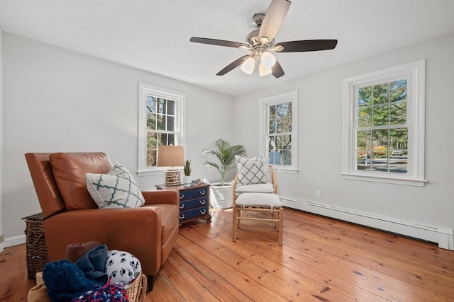 sitting room with a baseboard heating unit, ceiling fan, baseboards, and light wood-style flooring