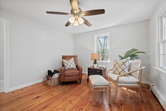 living area featuring light wood finished floors, a ceiling fan, and baseboards