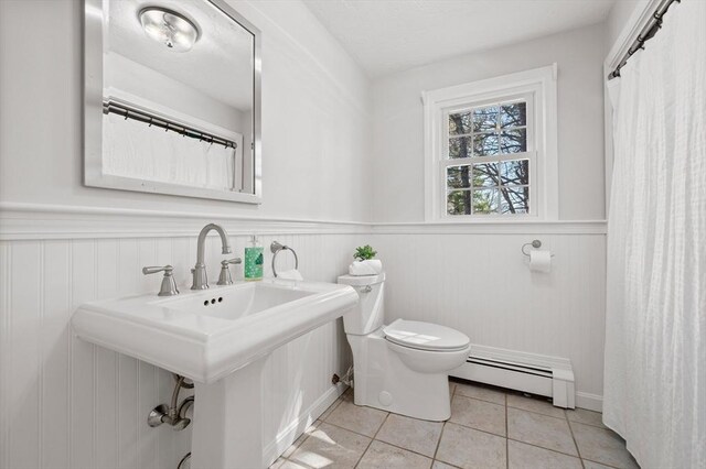 full bathroom with a wainscoted wall, a sink, toilet, tile patterned flooring, and a baseboard radiator