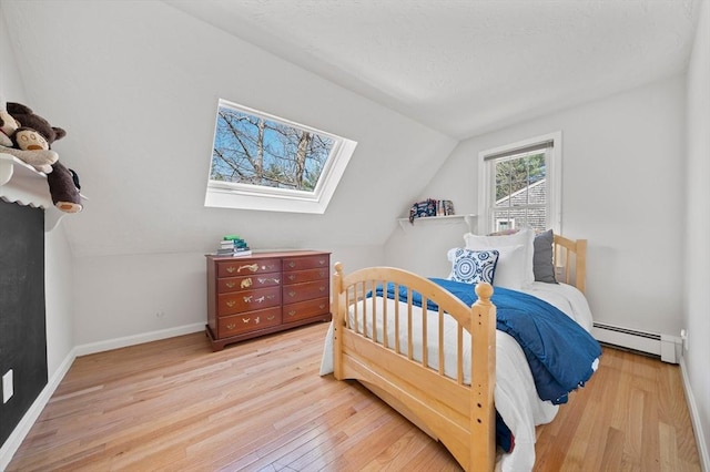 bedroom with a baseboard radiator, vaulted ceiling with skylight, wood finished floors, and baseboards