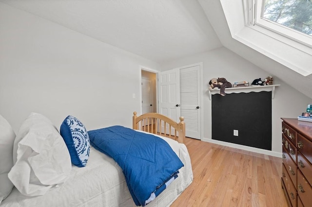 bedroom with baseboards, lofted ceiling, a closet, and light wood-style flooring