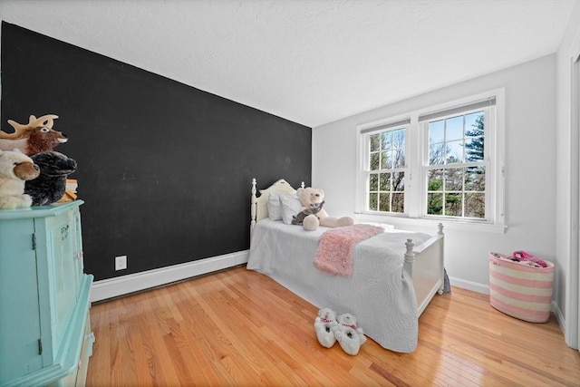 bedroom with a baseboard radiator, light wood-style floors, lofted ceiling, and baseboards