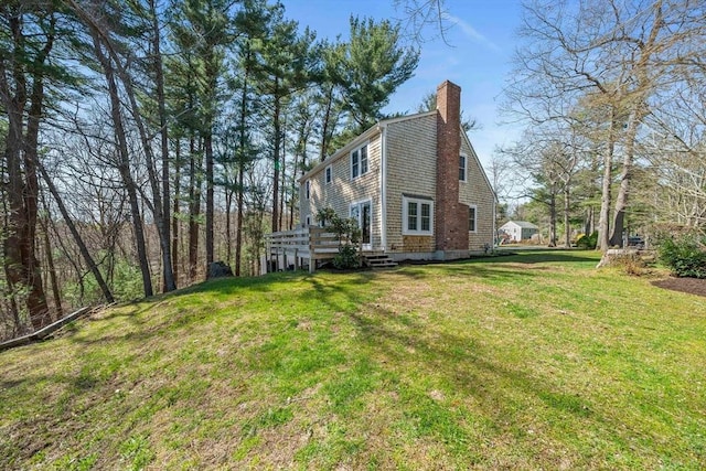 view of side of property with a wooden deck, a lawn, and a chimney