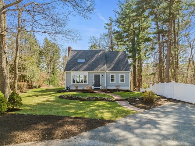 cape cod-style house featuring fence, a chimney, and a front yard