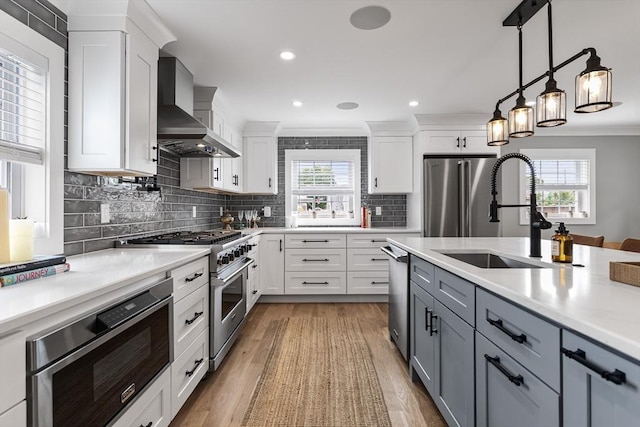 1 Wall St, Quincy, MA 02169 - kitchen featuring appliances with stainless steel finishes, wall chimney range hood, light countertops, white cabinetry, and light wood finished floors