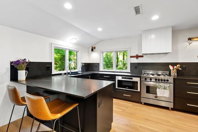 kitchen featuring appliances with stainless steel finishes, a peninsula, dark countertops, decorative backsplash, and recessed lighting