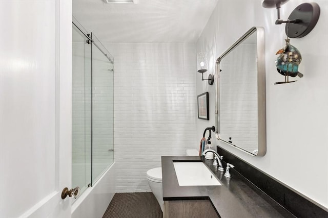 full bathroom with a sink, toilet, tile walls, and combined bath / shower with glass door