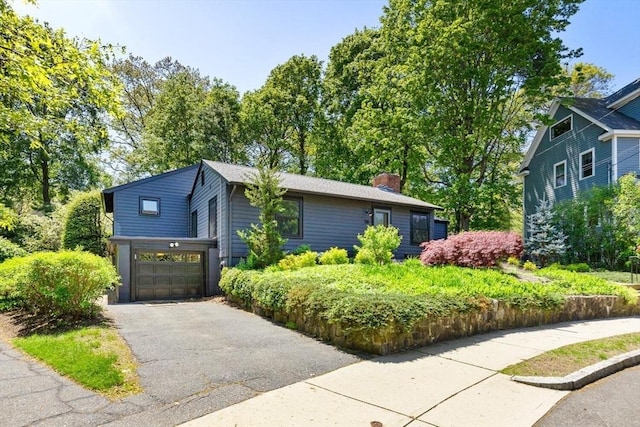 view of front of property featuring a garage, a chimney, and asphalt driveway