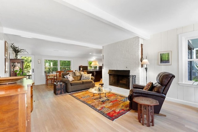 living area with light wood-type flooring, beamed ceiling, and a fireplace