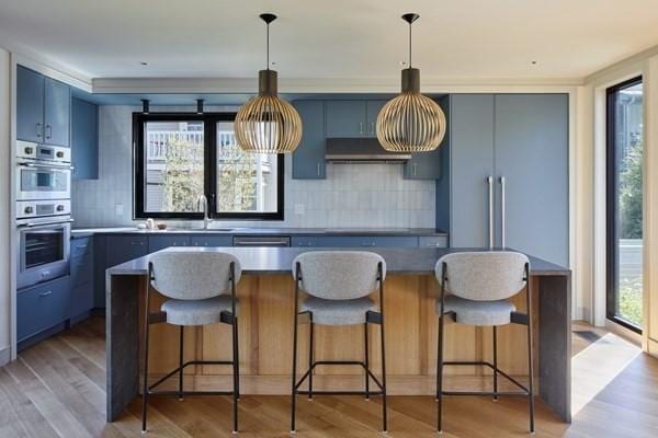 kitchen featuring light wood-type flooring, blue cabinetry, under cabinet range hood, and a sink