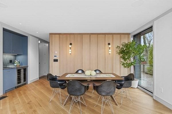 dining space featuring a baseboard radiator, beverage cooler, baseboards, light wood finished floors, and a dry bar