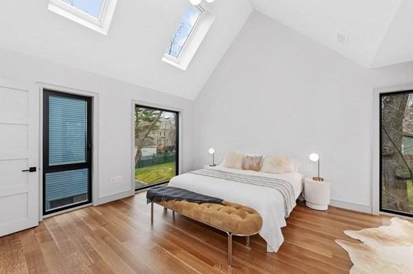 bedroom featuring access to exterior, a skylight, high vaulted ceiling, and wood finished floors