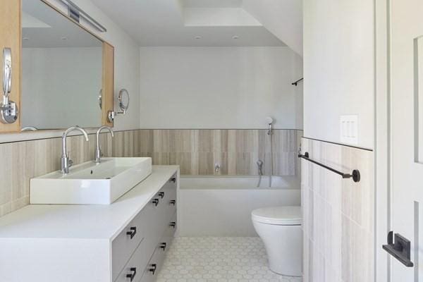 bathroom featuring wainscoting, toilet, a bathing tub, vanity, and tile walls