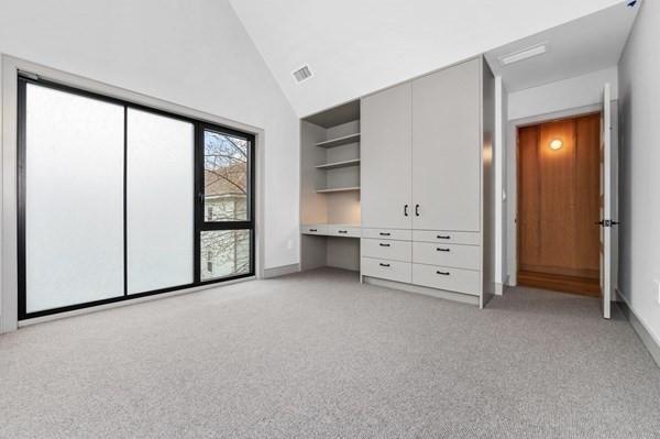 unfurnished bedroom with light carpet, high vaulted ceiling, built in study area, and visible vents