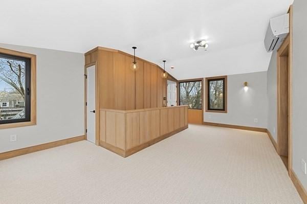 interior space featuring light carpet, vaulted ceiling, baseboards, and a wall mounted AC