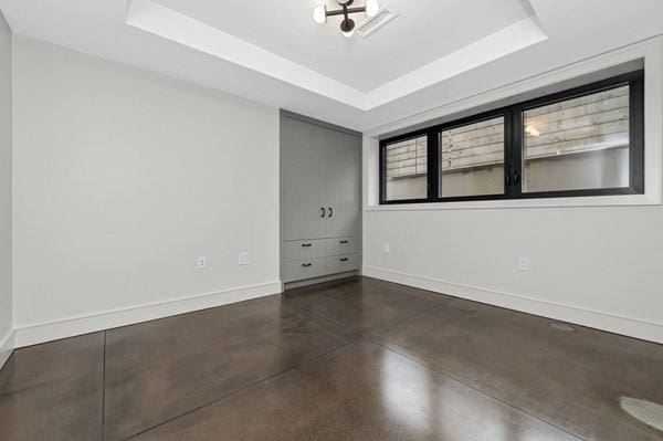 spare room with baseboards, concrete floors, and a tray ceiling