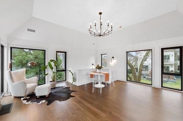 living area with lofted ceiling, a notable chandelier, visible vents, and wood finished floors