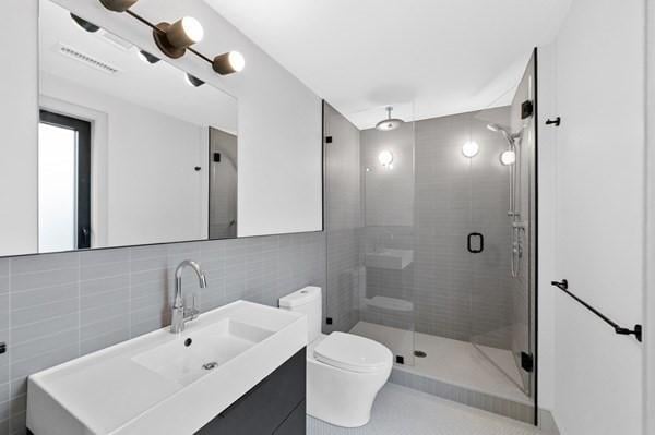 full bath with tile walls, visible vents, toilet, a shower stall, and vanity