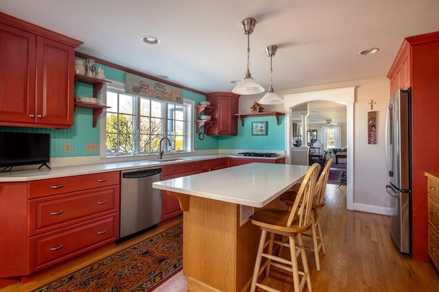 kitchen with pendant lighting, sink, light wood-type flooring, a kitchen island, and stainless steel appliances