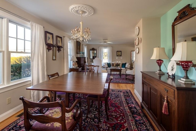 dining space with ceiling fan with notable chandelier and light hardwood / wood-style floors