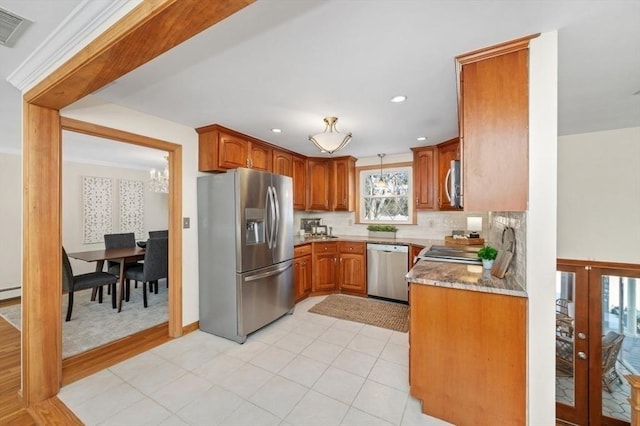 kitchen with appliances with stainless steel finishes, decorative light fixtures, a baseboard radiator, backsplash, and light stone counters