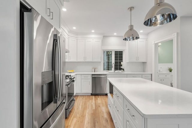 kitchen with light countertops, appliances with stainless steel finishes, white cabinets, a sink, and light wood-type flooring