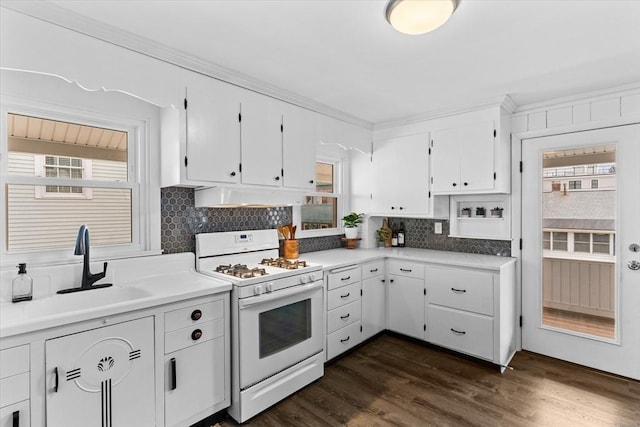 kitchen featuring white gas stove, white cabinetry, under cabinet range hood, tasteful backsplash, and a sink