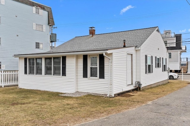 view of side of home featuring a lawn, a shingled roof, and fence