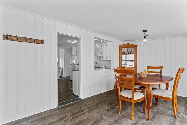 dining room with crown molding, a decorative wall, and dark wood-style floors