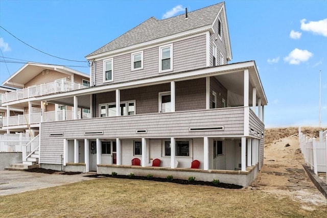 view of front facade with fence, a shingled roof, and a balcony
