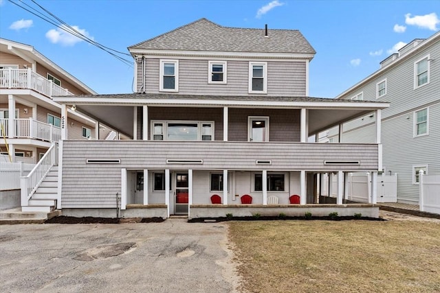 view of front of property with fence, a shingled roof, a balcony, and a front lawn
