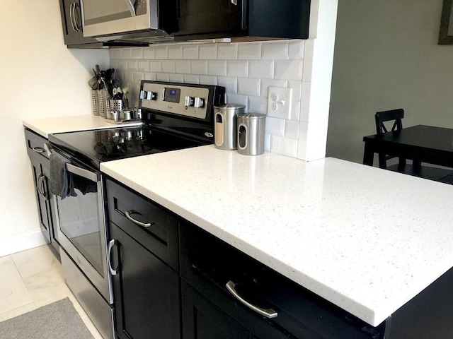 4 Emerson Gardens Rd Unit 4, Lexington, MA 02420 - kitchen featuring stainless steel appliances, dark cabinets, tasteful backsplash, light stone counters, and light marble finish floors