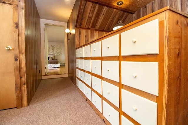 hallway featuring lofted ceiling, light colored carpet, wooden ceiling, and wooden walls