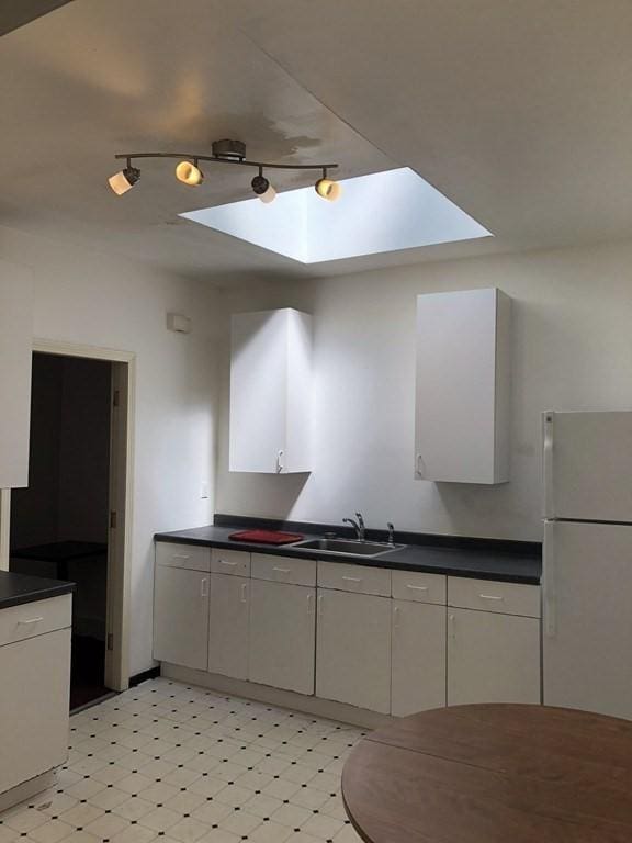 kitchen with white refrigerator, a skylight, white cabinetry, and sink