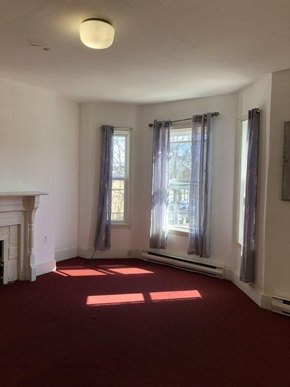 unfurnished living room with carpet, a tiled fireplace, and a baseboard heating unit