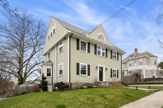 view of front of home with central AC, fence, and a front lawn
