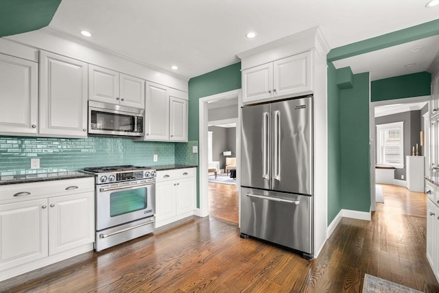 kitchen with white cabinets, stainless steel appliances, dark wood-style floors, baseboards, and backsplash