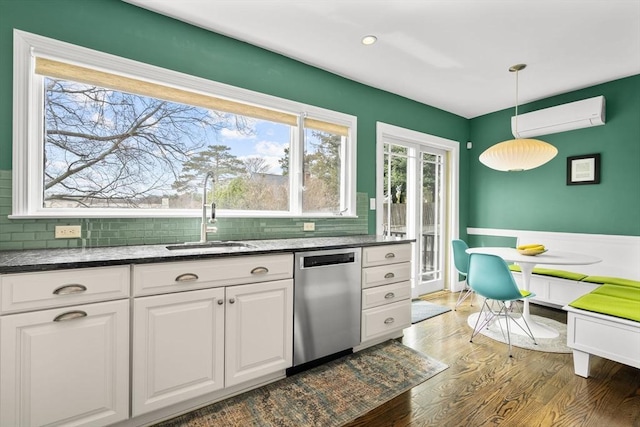 kitchen with a sink, a wall mounted AC, stainless steel dishwasher, white cabinets, and wood finished floors
