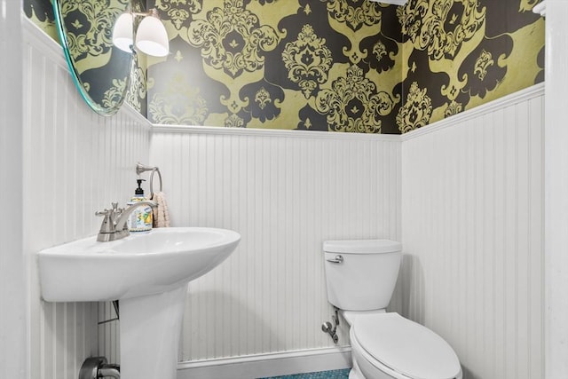bathroom featuring wallpapered walls, a wainscoted wall, and toilet
