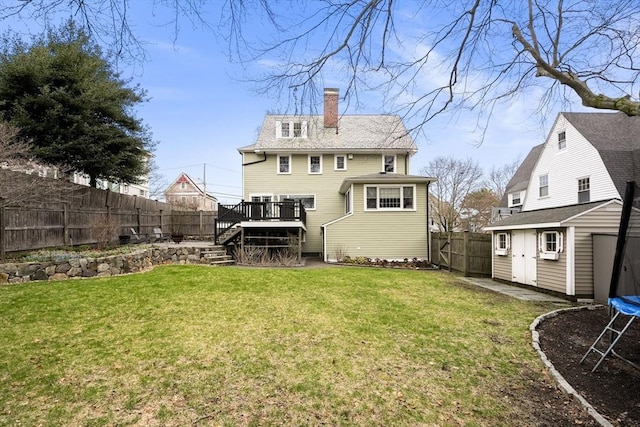 rear view of house featuring an outdoor structure, a trampoline, a storage unit, a deck, and a fenced backyard